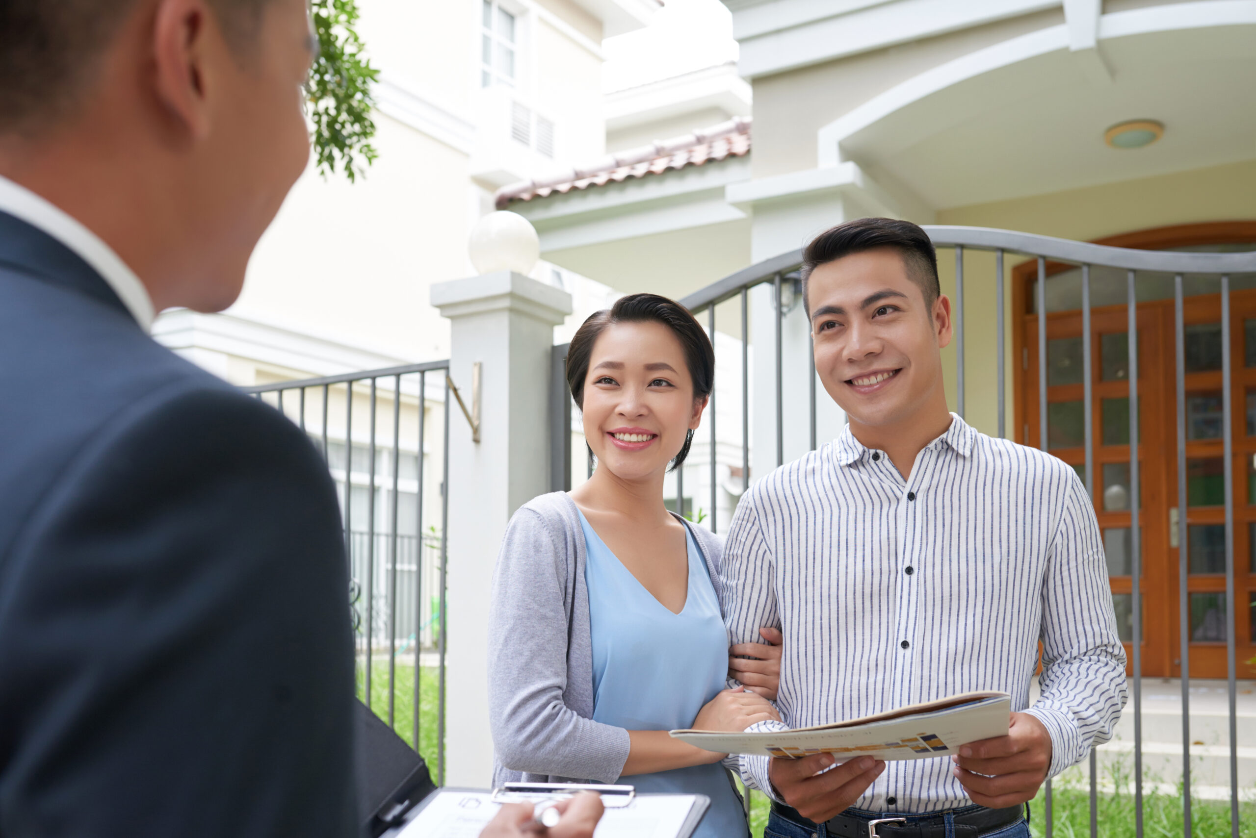 Cheerful young Vietnamese family talking to real estate agent in front of house